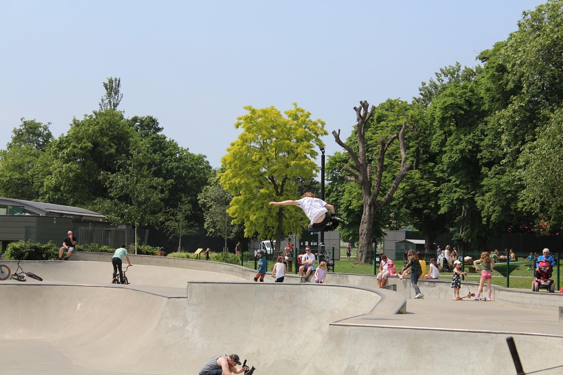 People roller skating on the pavement in the park surrounded by trees, with skateboarders in the foreground