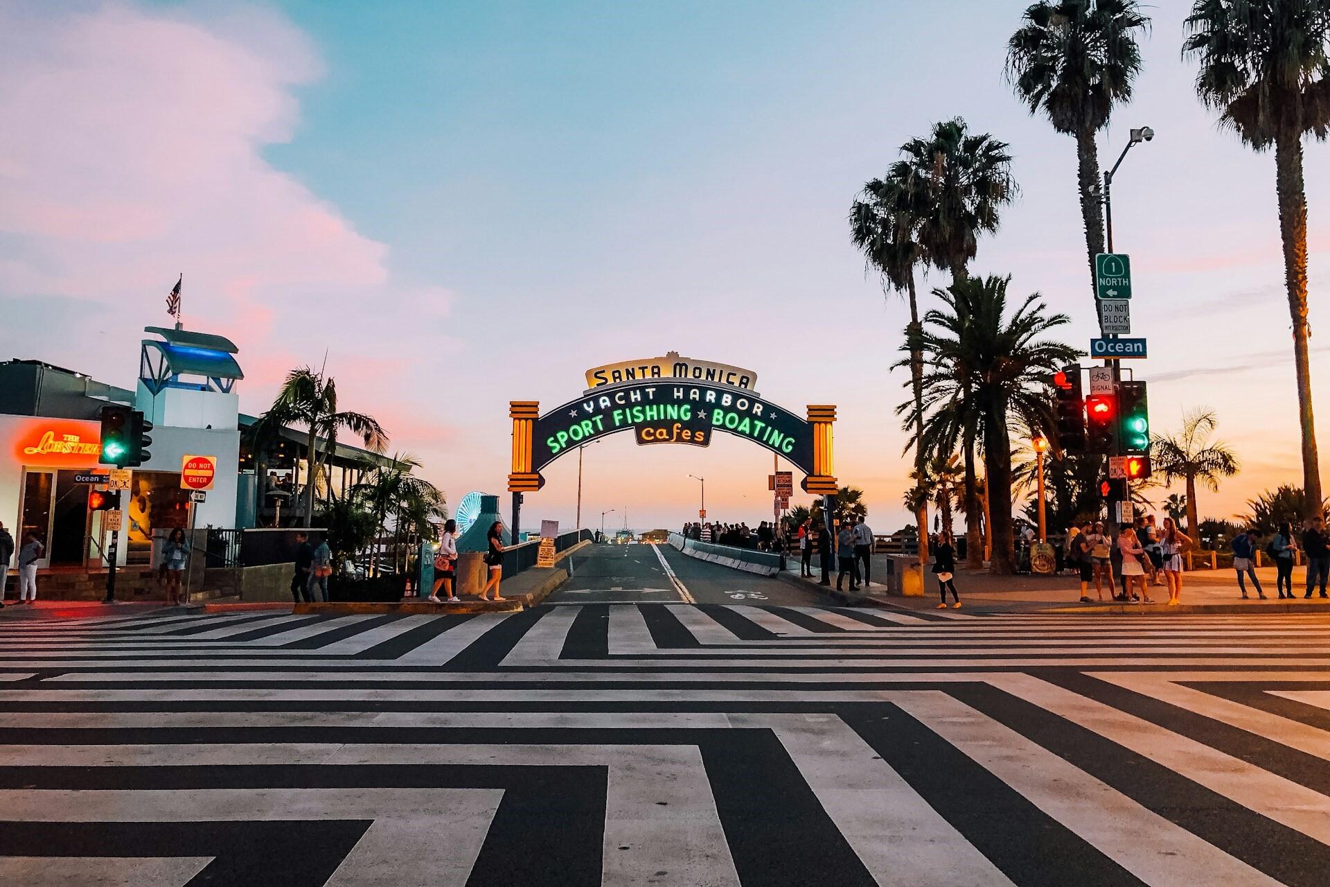 Santa Monica Pier entrance at sunset with palm trees and a striped crosswalk