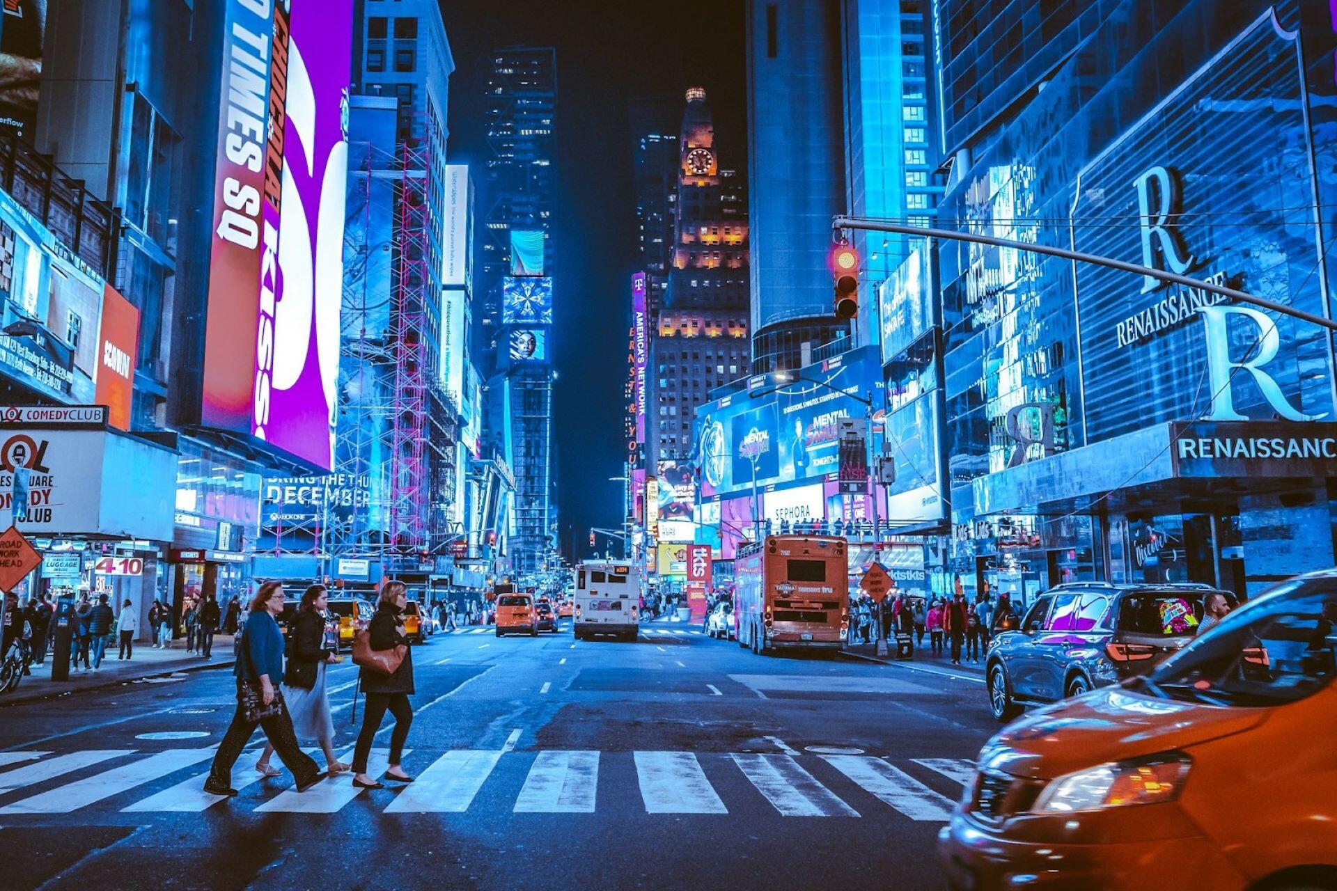 Times Square at night with illuminated billboards, traffic, pedestrians, and tall buildings