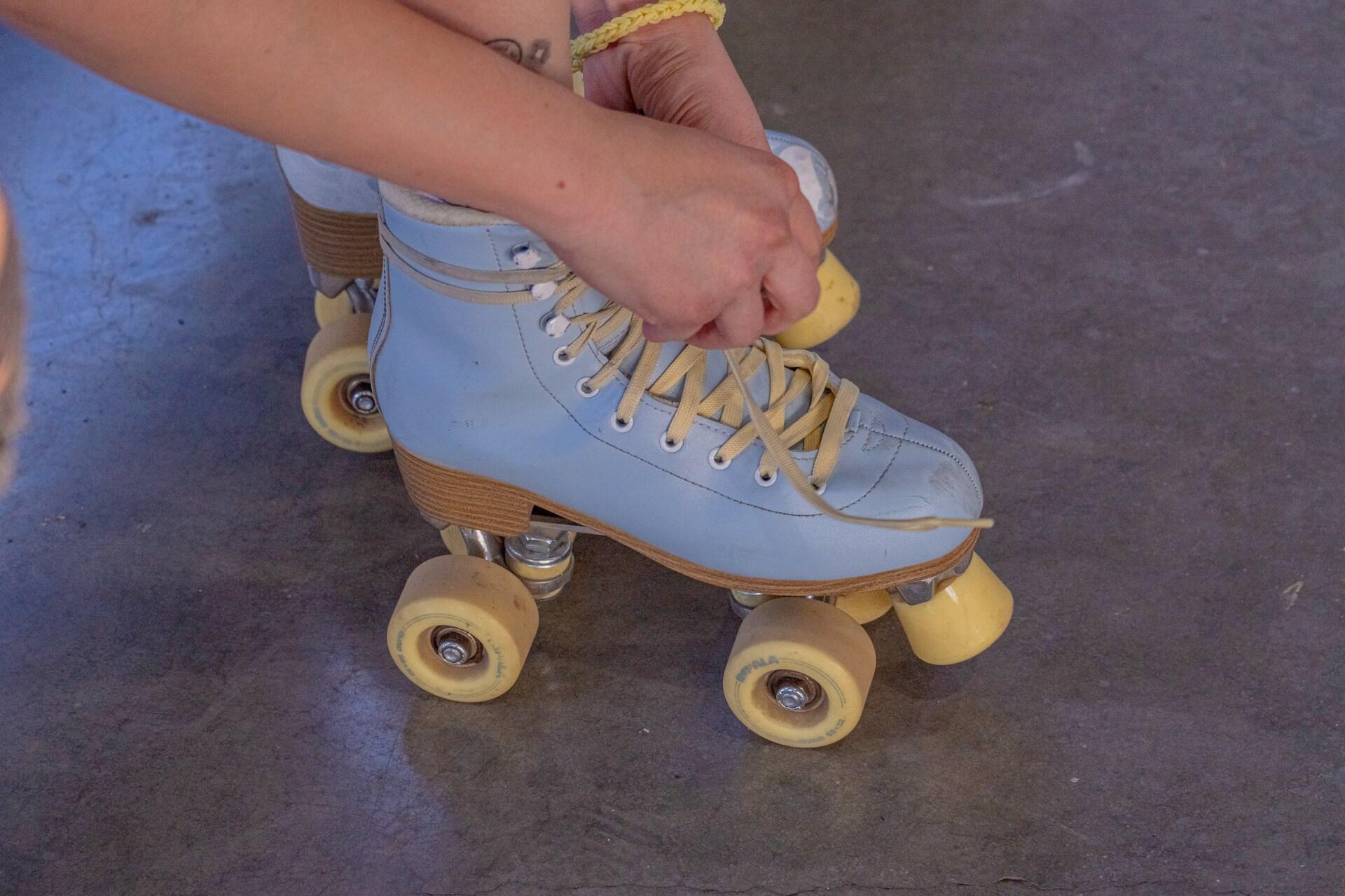 Person tying the laces of a light blue roller skate with yellow wheels