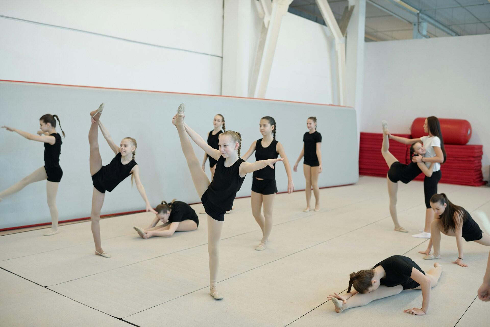 Kids dressed in black dancing and stretching with a choreographer in the back.