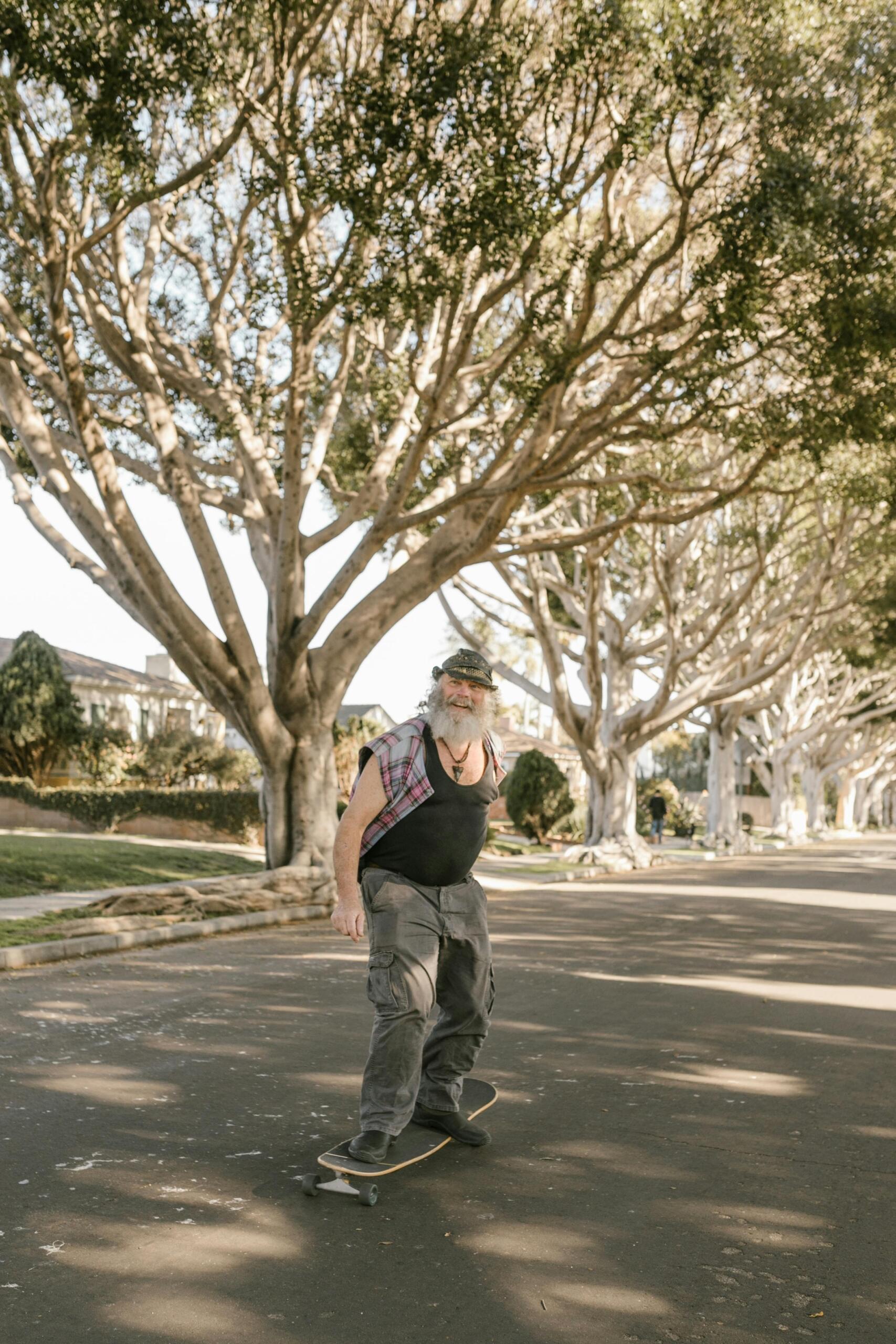 An elderly man skateboarding near trees, demonstrating agility and confidence in his movements.