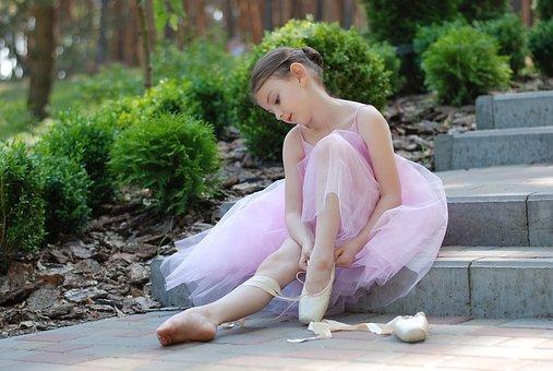 A young girl sitting on a step while putting on her ballet shoes