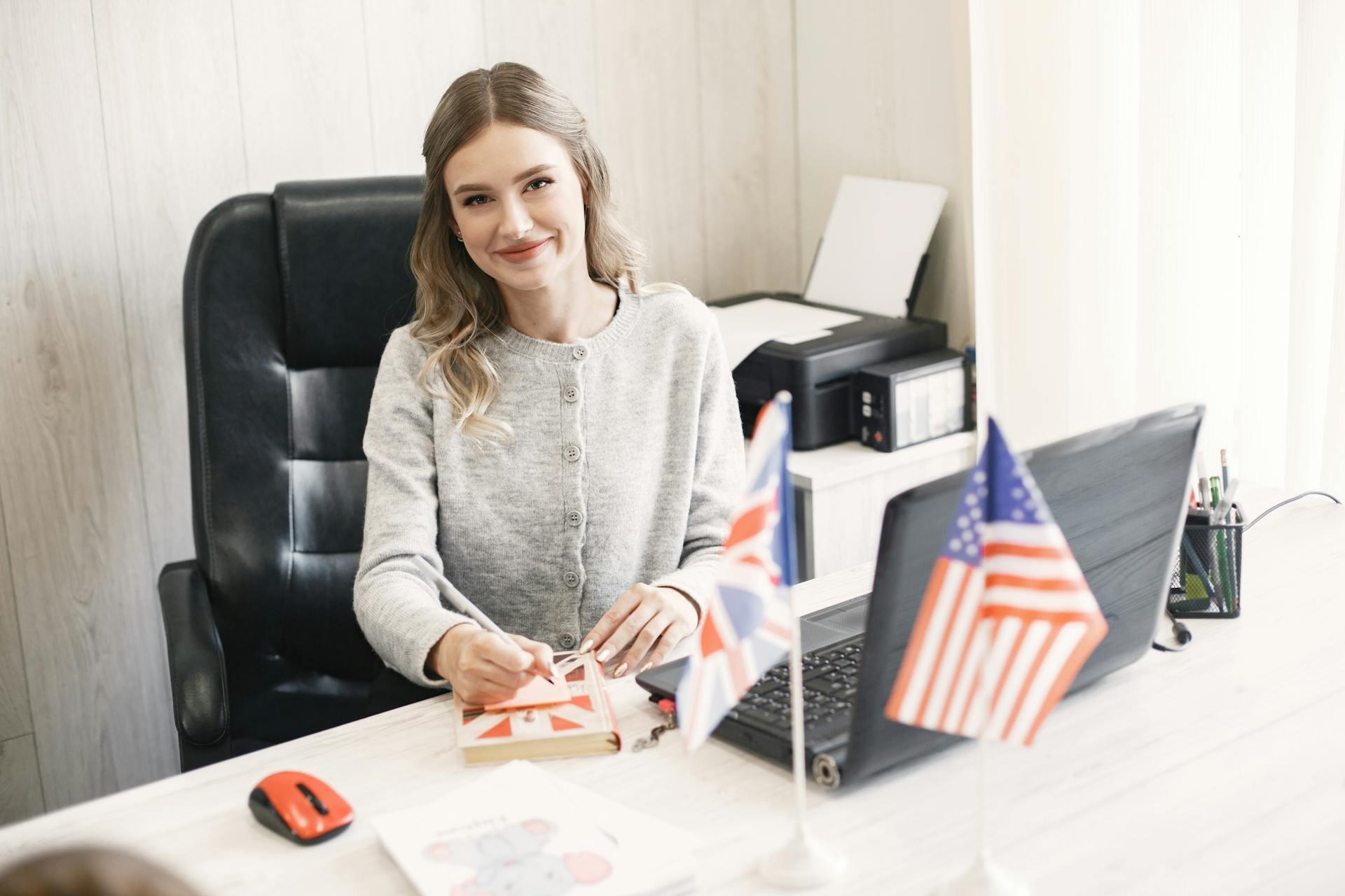 A girl smiling at her desk with a UK and US flag in front of her.