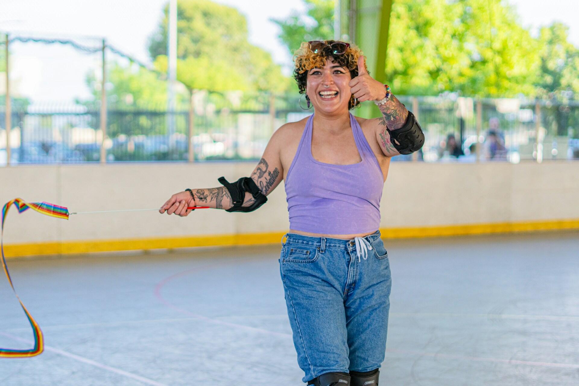 A girl with tattoos and a purple top on giving a thumbs up while roller skating.