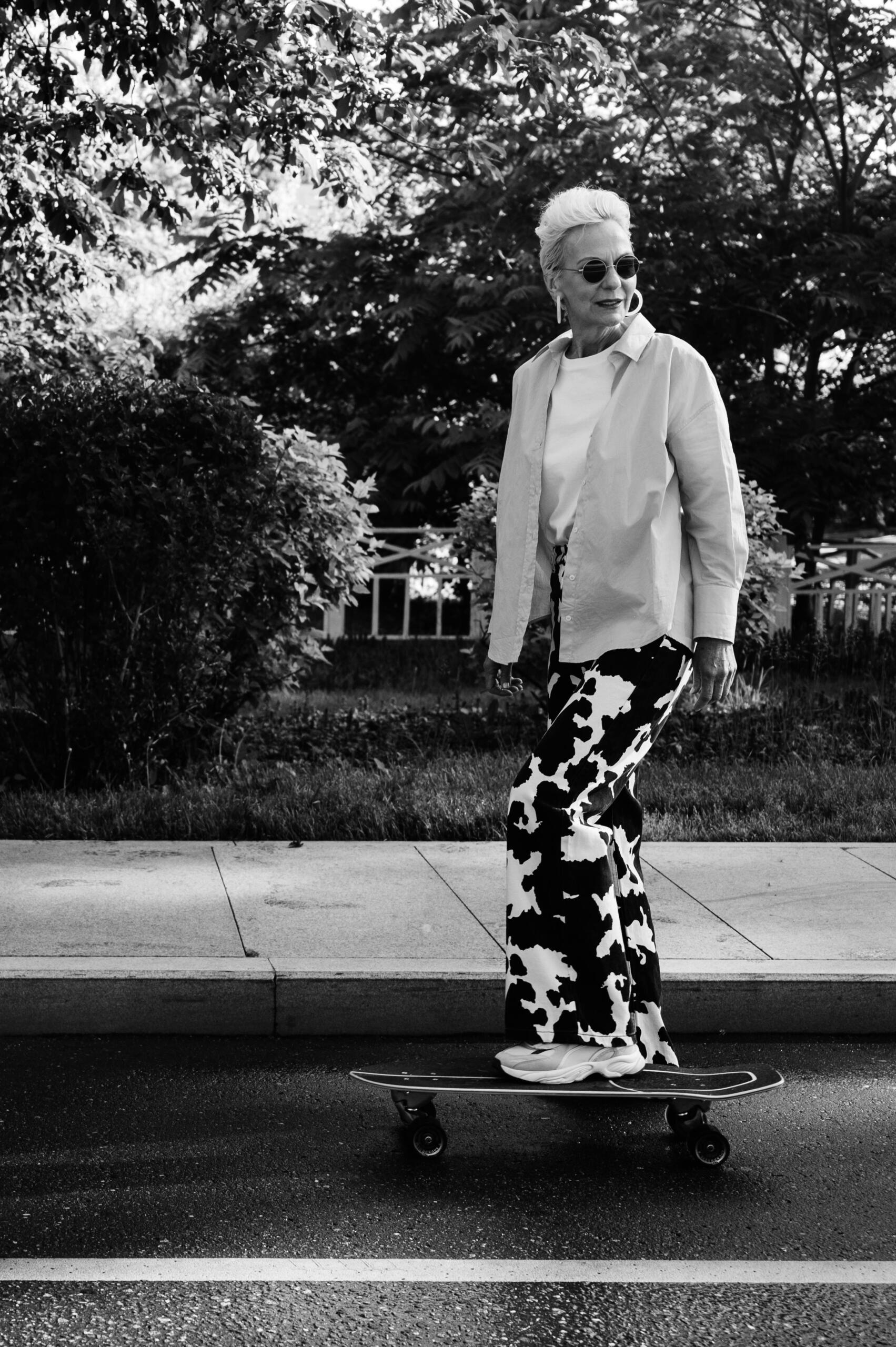 A grayscale photo of an elderly woman confidently riding a skateboard, showcasing her adventurous spirit.