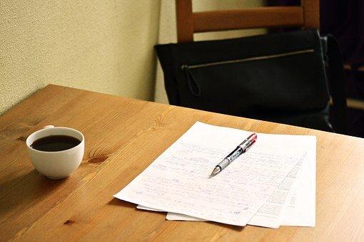 A set of papers, a pen, and a cup of coffee placed on a wooden table