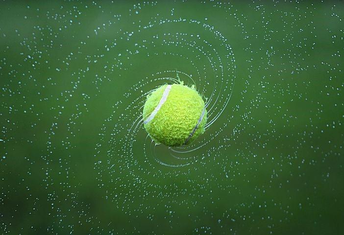 A wet tennis ball swirling mid-air sprinkling water droplets