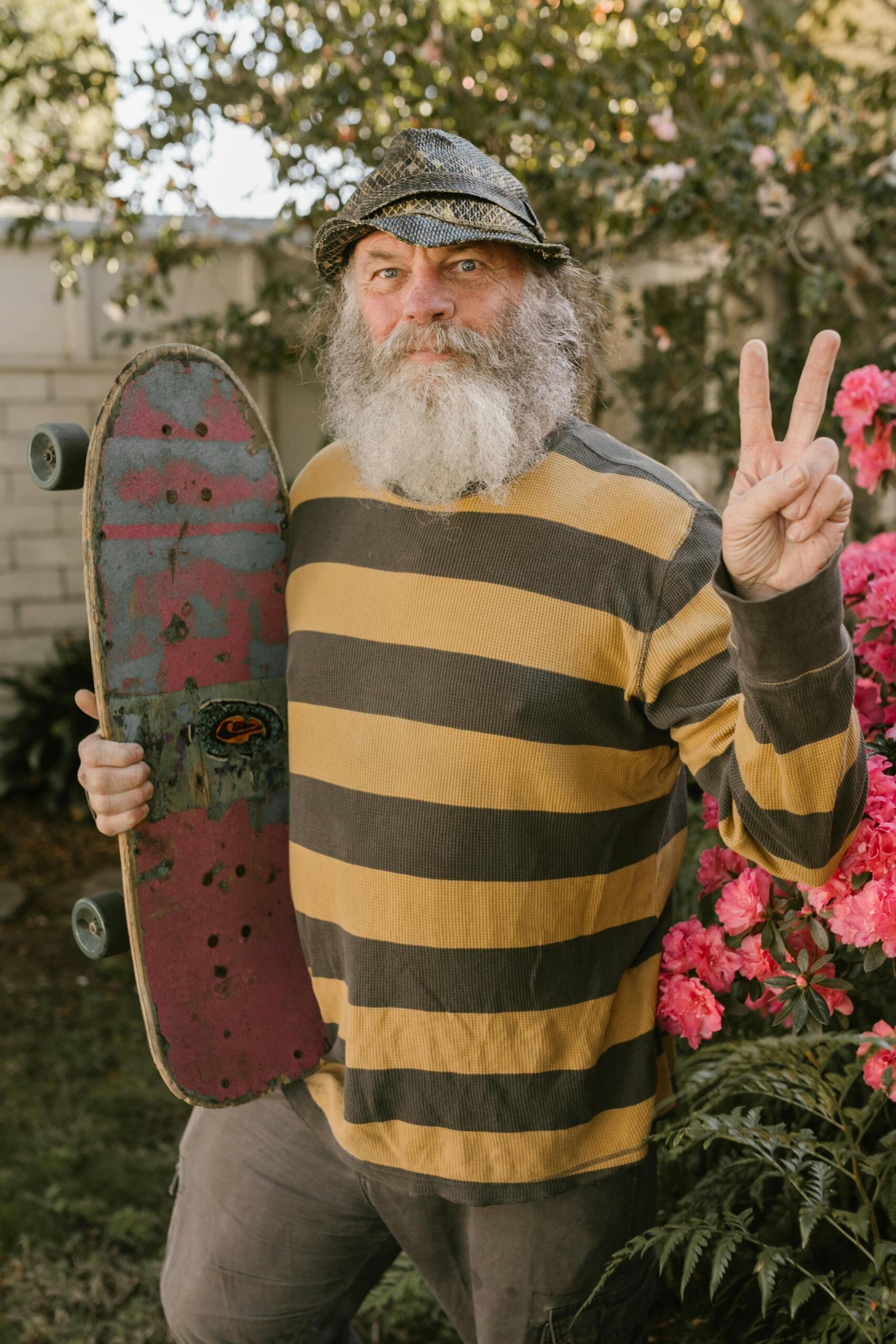 A man in a yellow and black striped long-sleeve shirt holding a brown wooden skateboard.