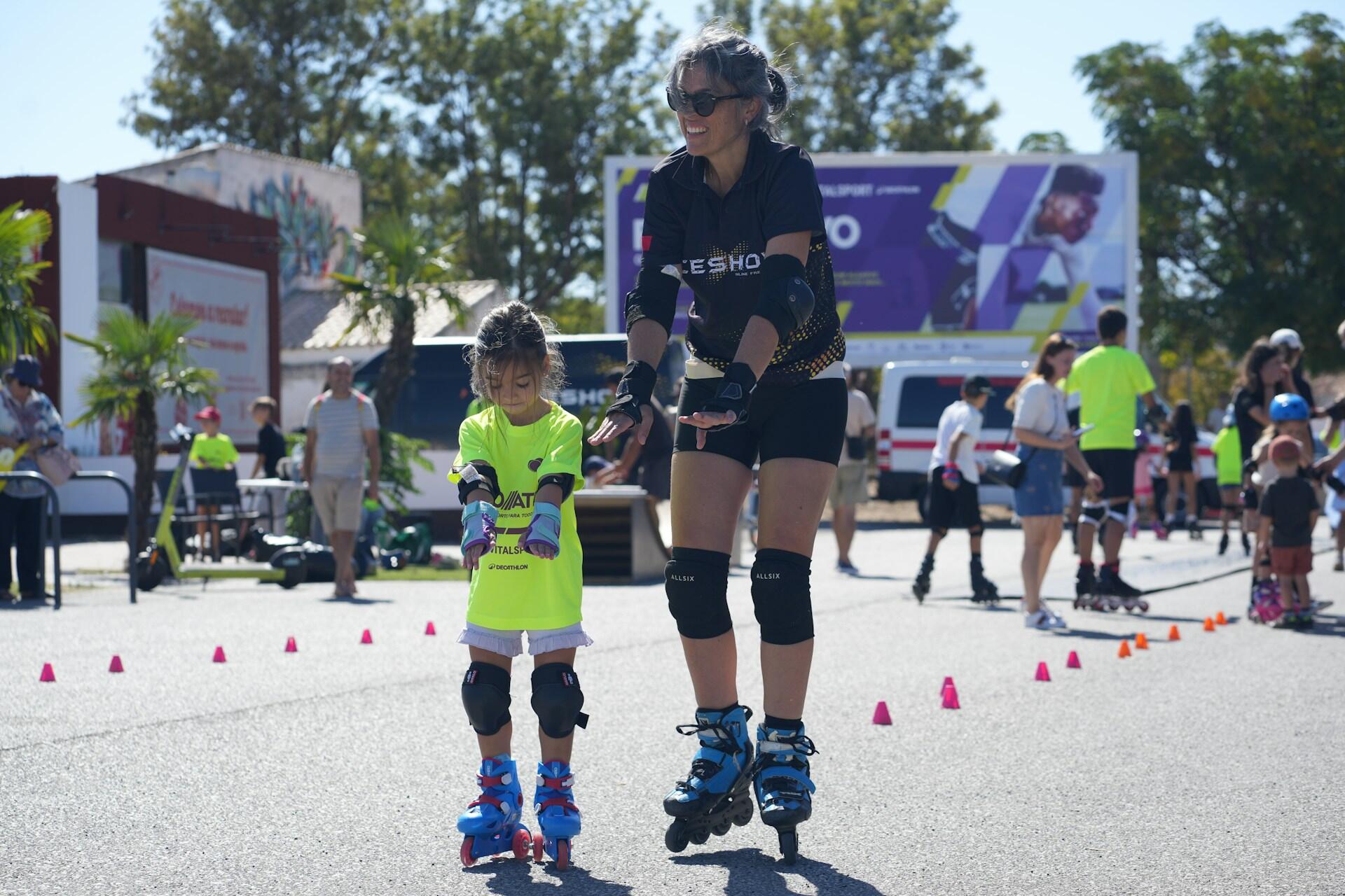 A little girl in a bright yellow shirt learning to roller skate next to a women roller skating.