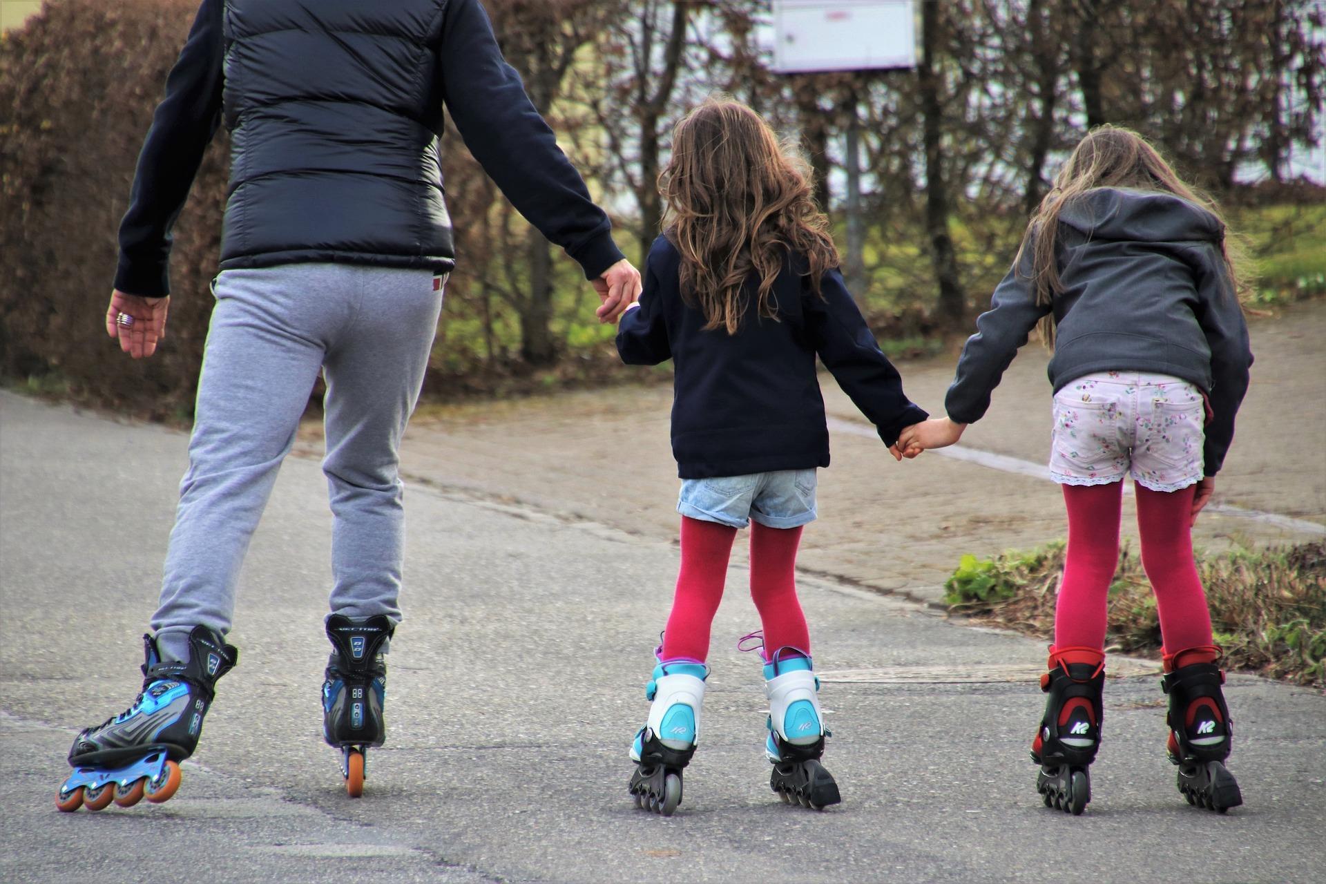 A man and two young girls holding hands while roller skating