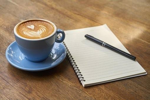 A coffee with latte art, a pen, and a notebook