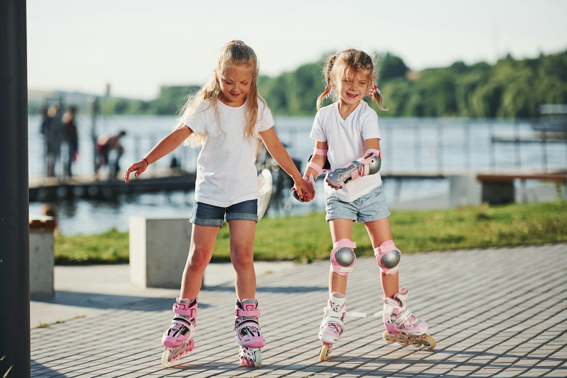 Two young girls holding hands and roller skating.