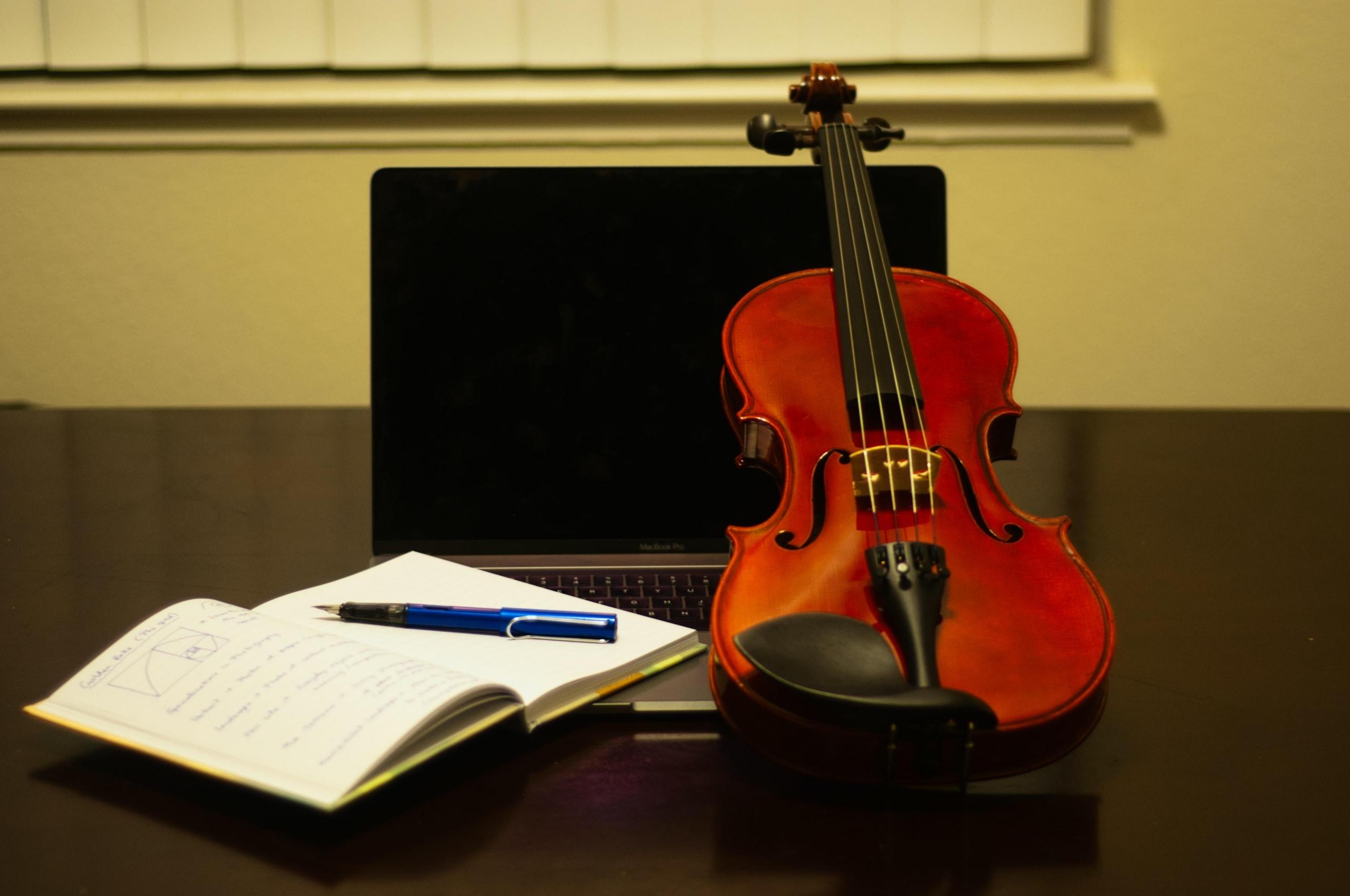 A brown violin is placed on the table along with a pen and a notebook