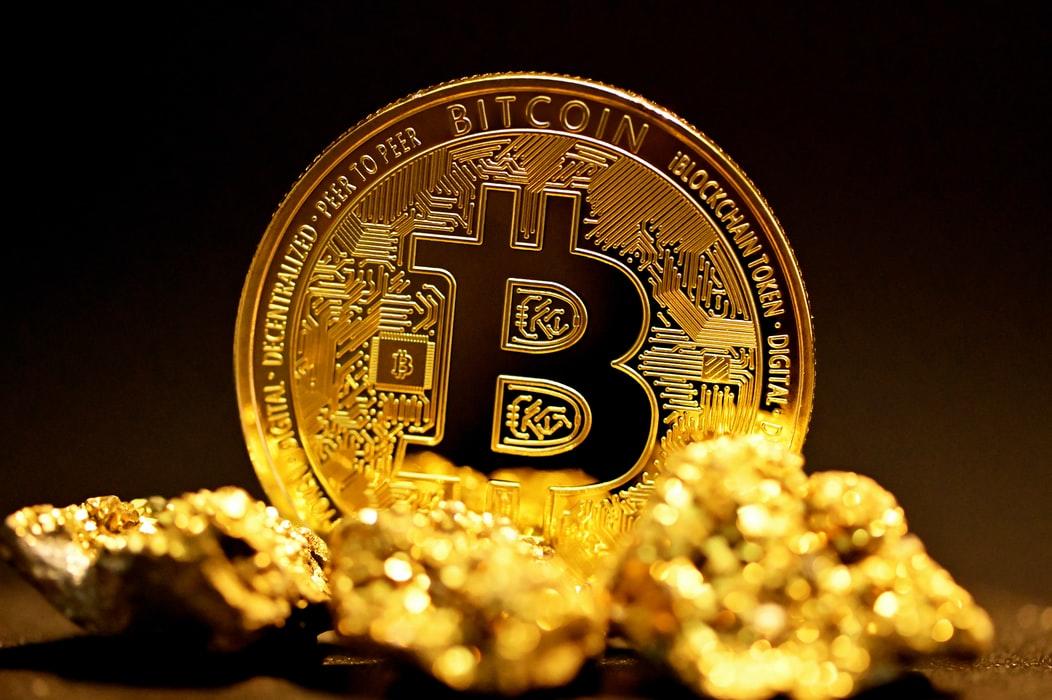 A single bitcoin surrounded by raw gold pieces
