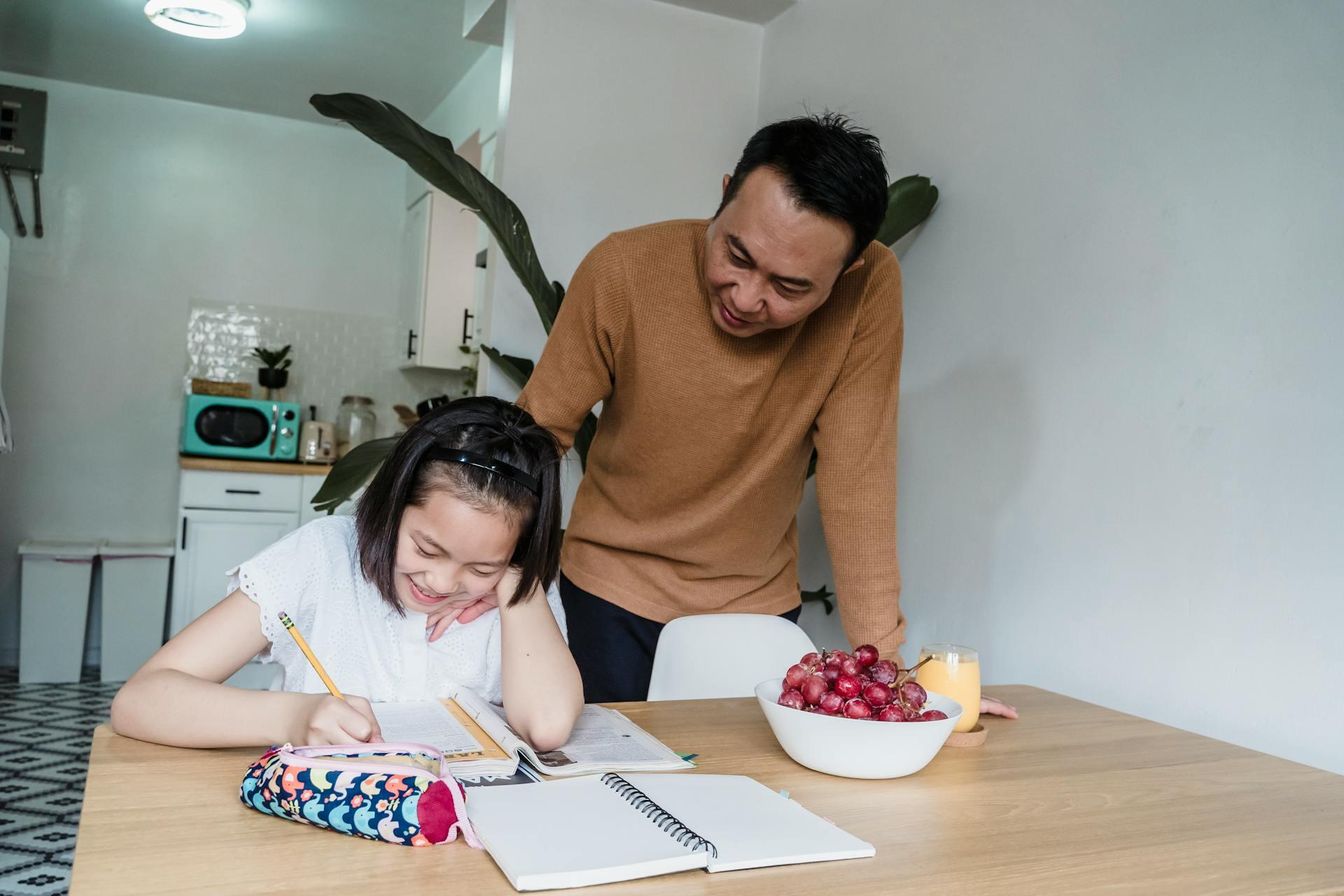 A young girl doing homework at the table and a man helping her.