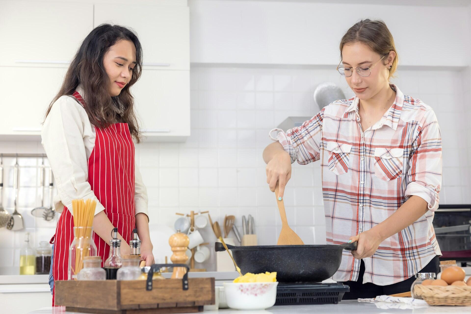 A girl cooking and a tutor in a red apron supervising.