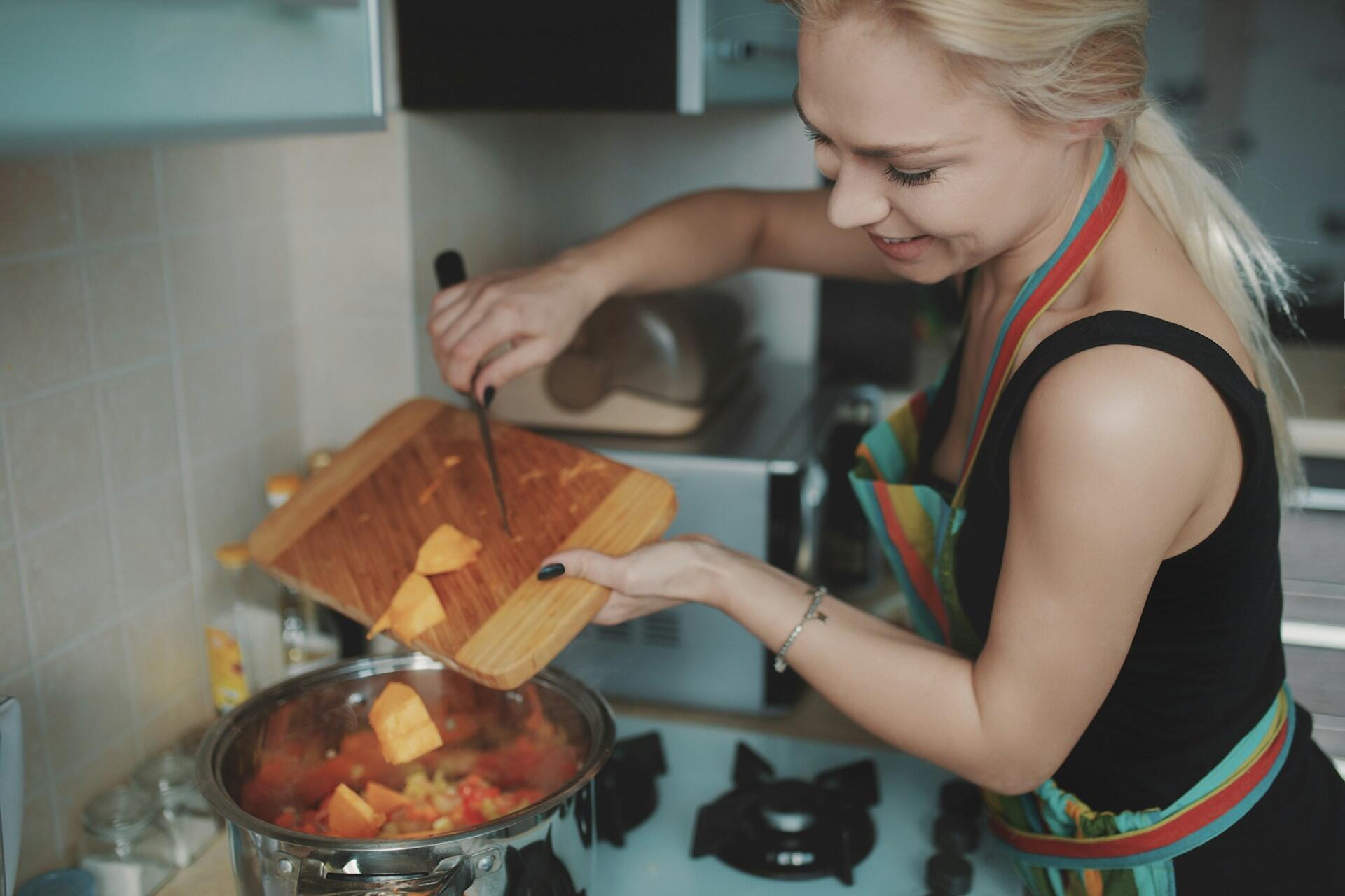 A lady putting ingredients in a soup pot.