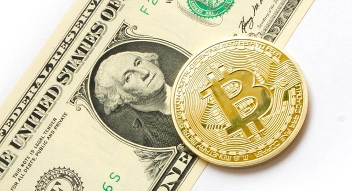 There is a bitcoin above the US dollar with a shiny light brown color