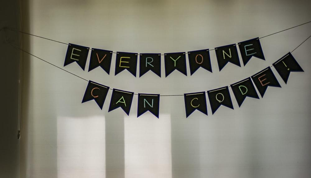 Small black letter flags that say "everyone can code" hanged in front of a white wall