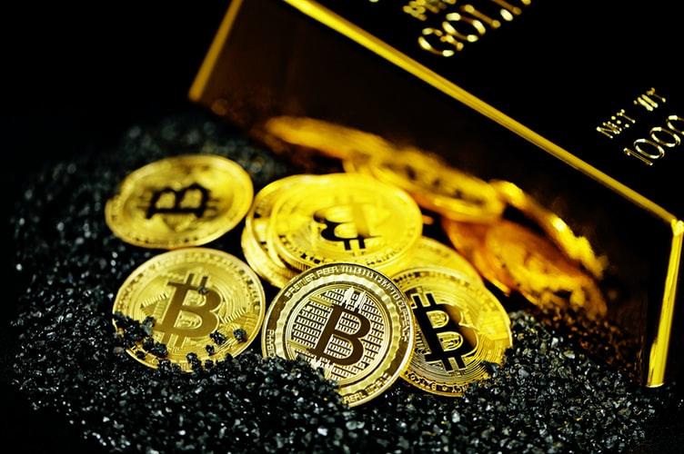 A pile of Bitcoins on black crystals next to gold bullion
