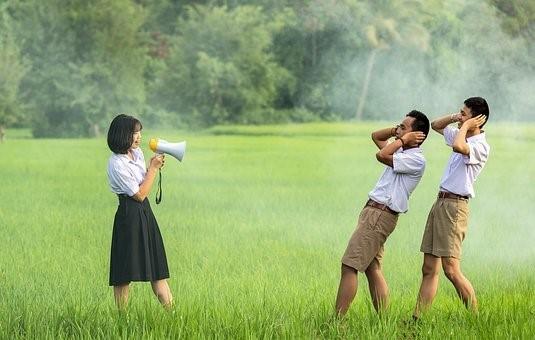 A girl speaking in a horn while two boys hold their ears