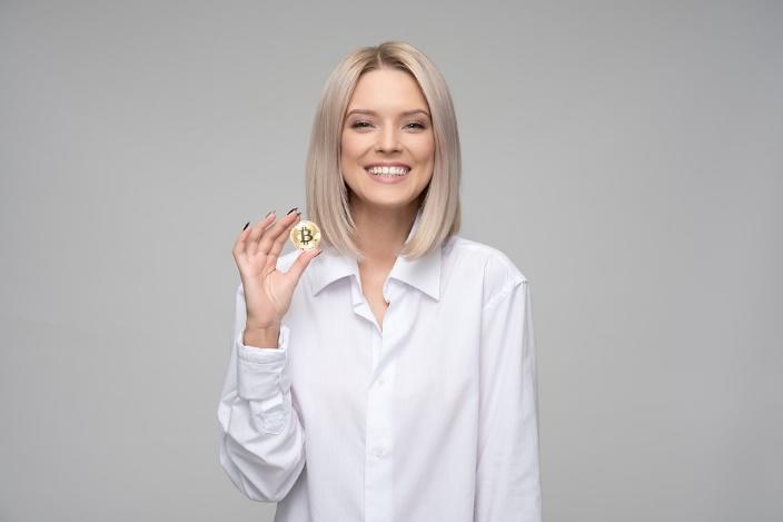 A lady wearing white attire shows a coin that features Bitcoin