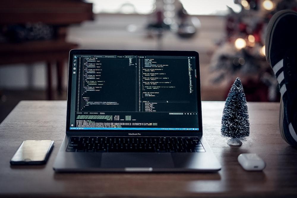 A coding display laptop placed on a table with a Christmas tree toy, an iPhone, and an AirPods case