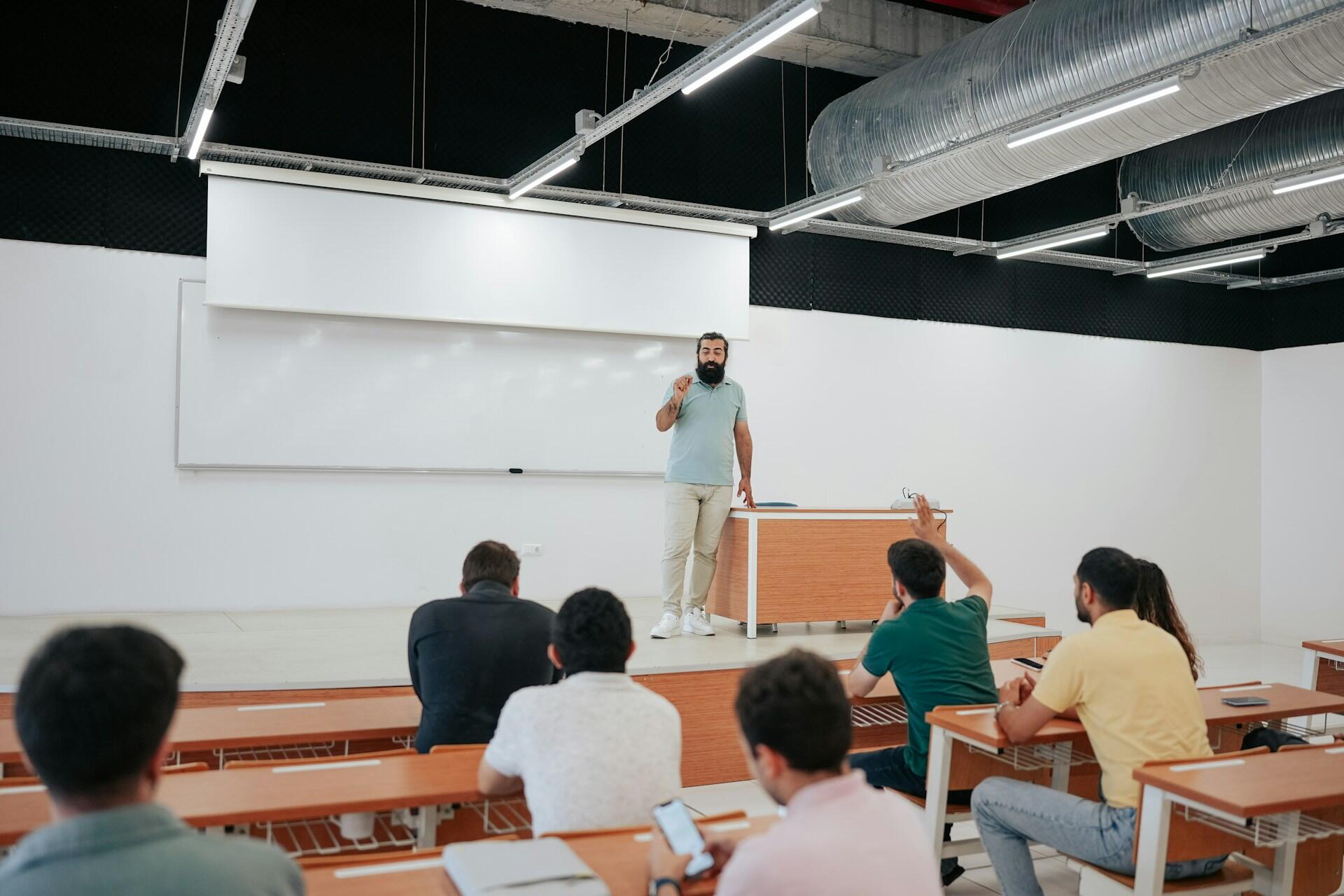 A professor pointing at a student and students sitting in a classroom.