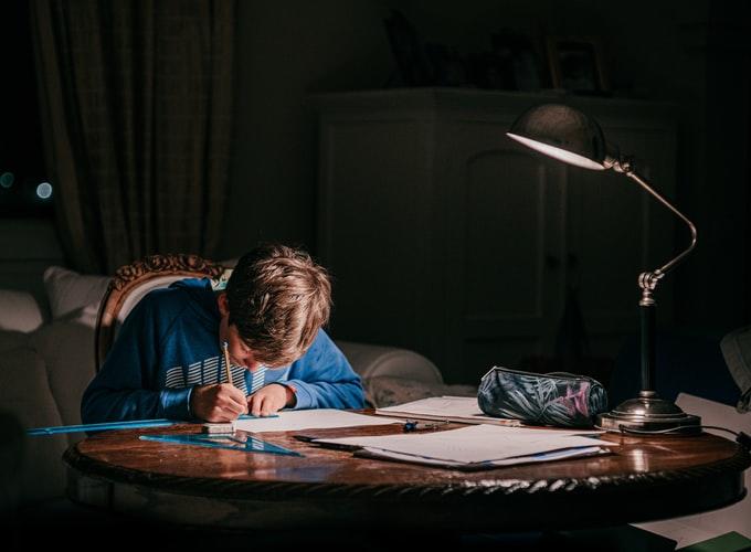 A boy studying under the shade of a lamp
