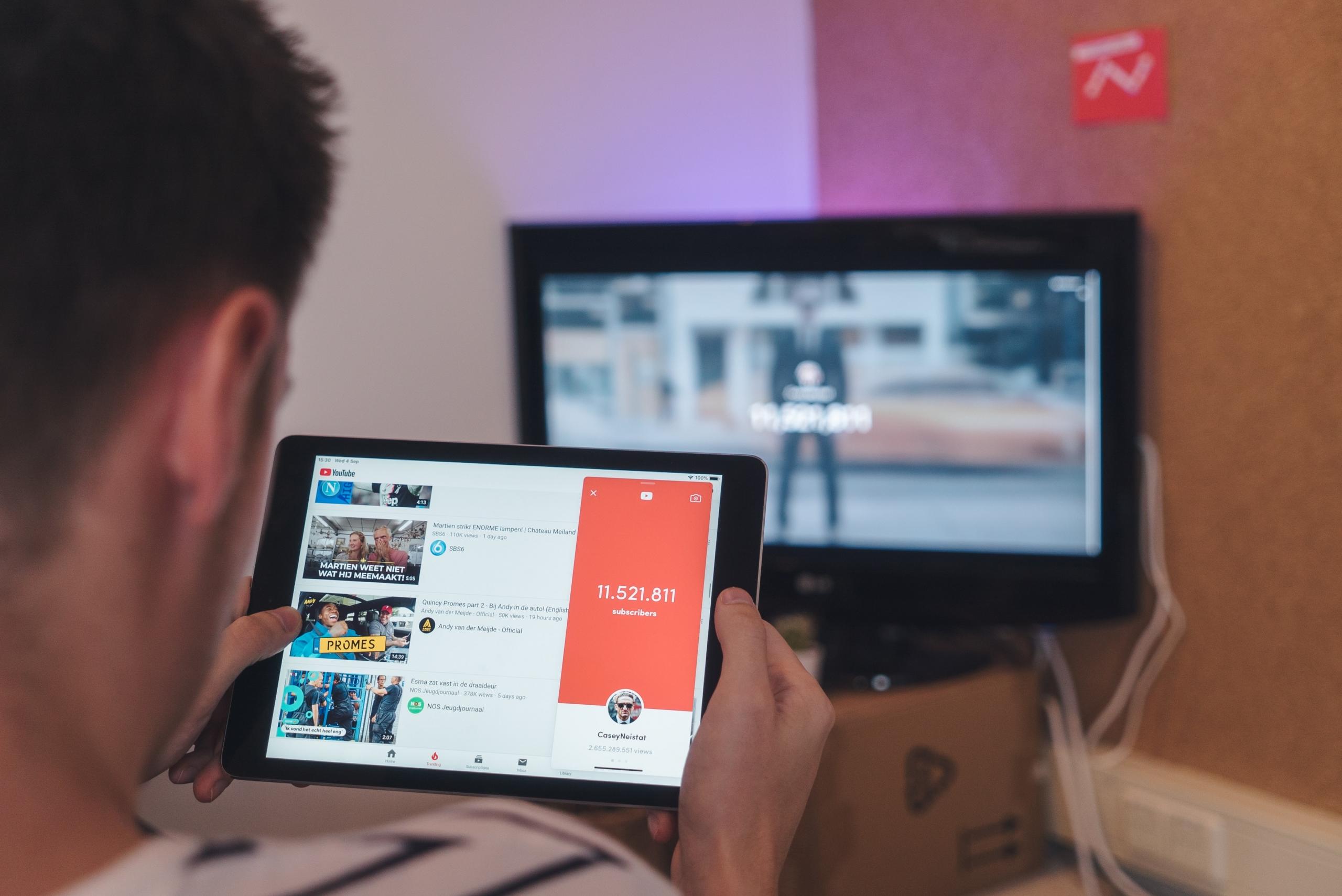 Man browsing YouTube on his tablet while sitting in front of a TV