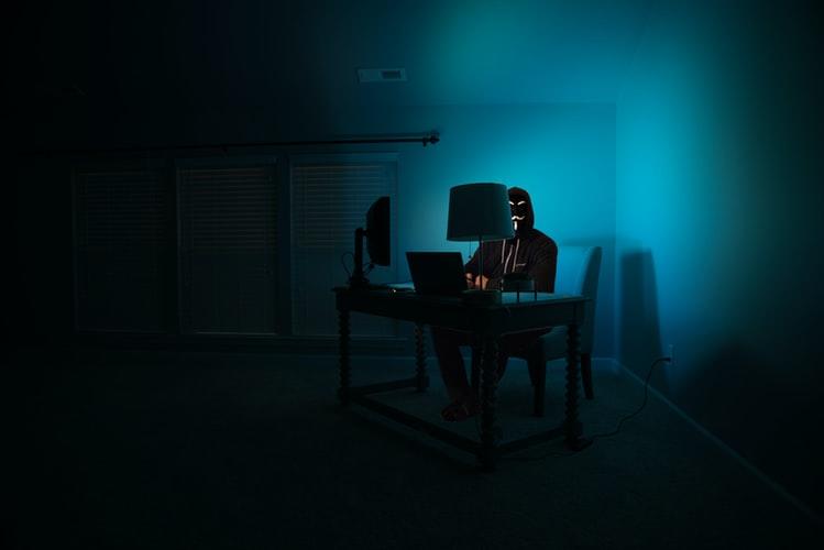 A man disguised as an anonymous hacker using a computer