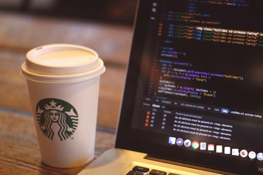 A Starbucks cup placed next to a laptop with the coding on the screen