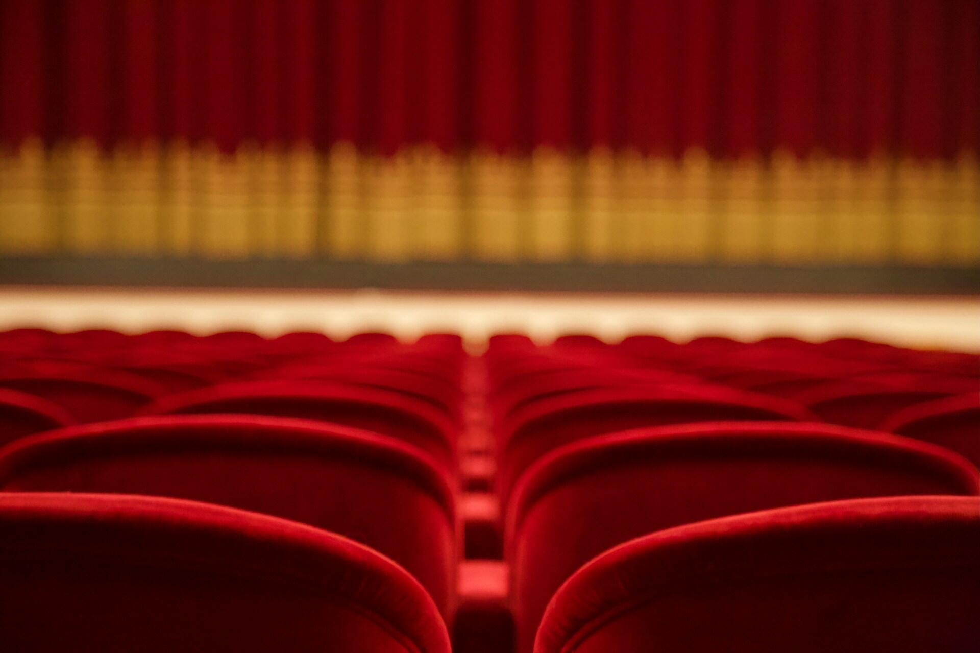 Rows of empty red theatre seats inside an auditorium.