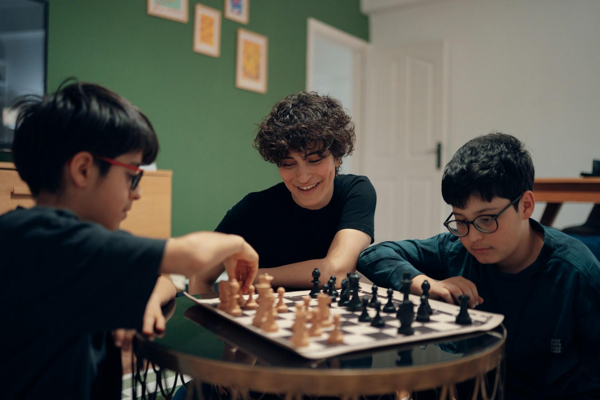 Three young boys playing chess at a table/