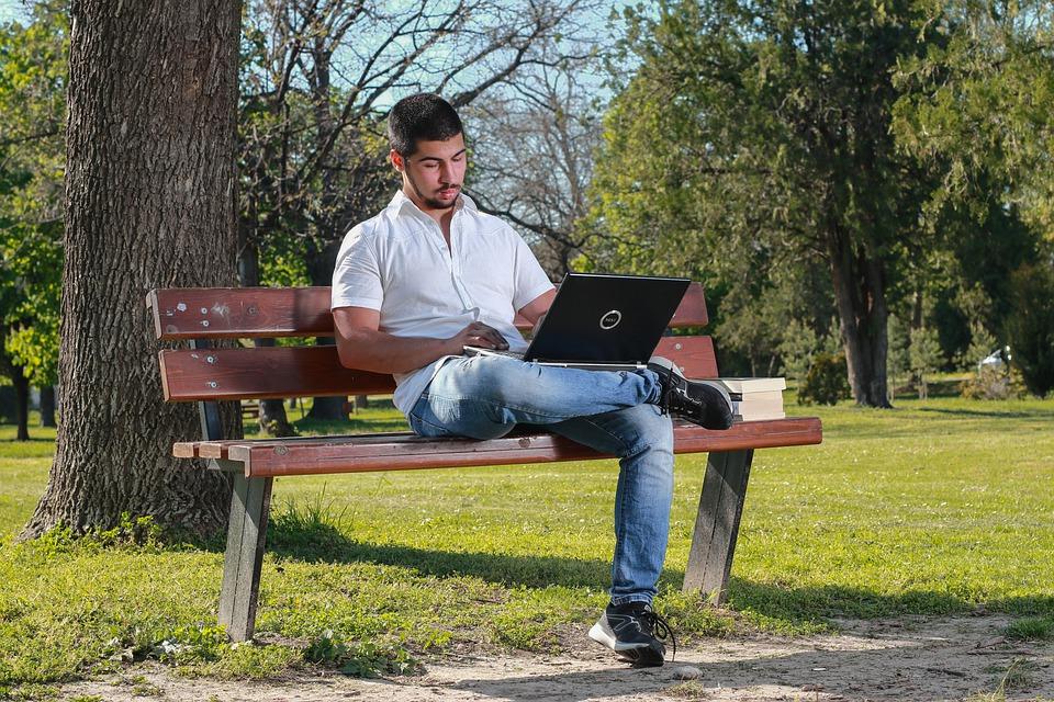 A man working on his laptop while sitting on a park bench