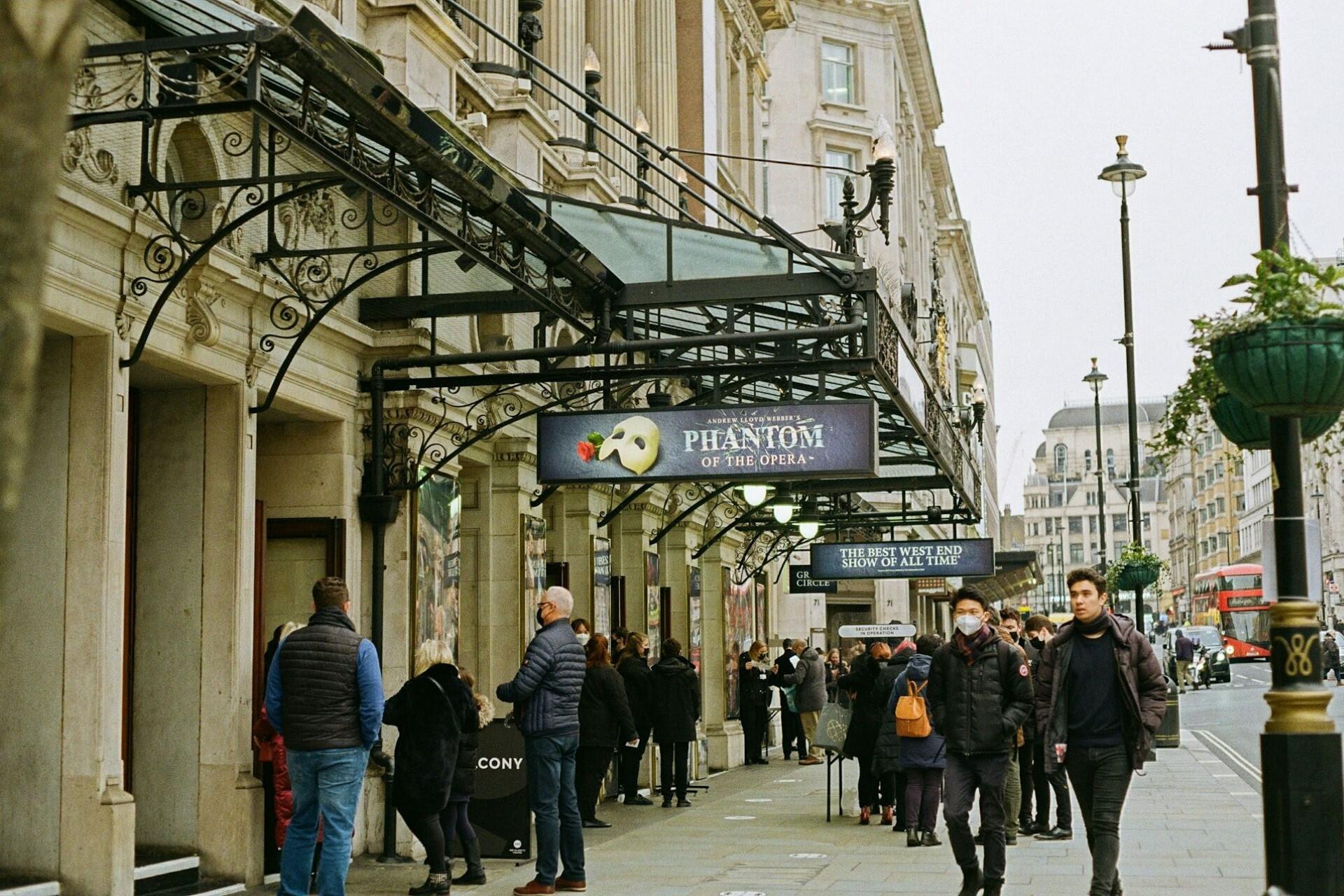 People queuing outside a West End theatre with signage for The Phantom of the Opera.