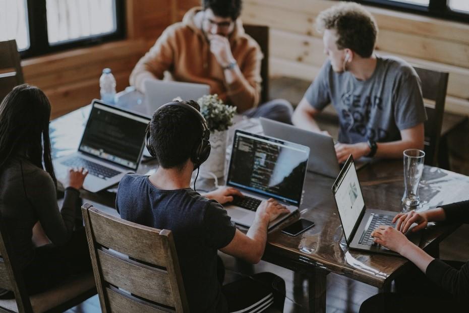 A room with a table, laptops, and a group of business graduates working on a group project