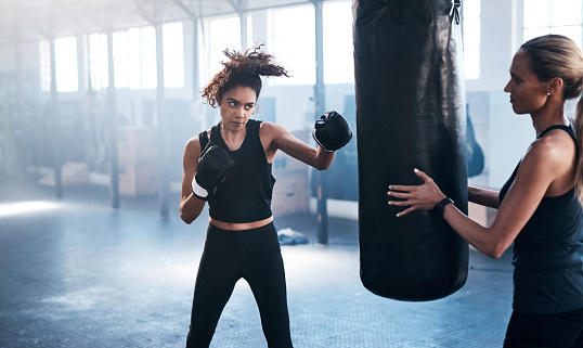 A teenager practicing on a punching bag under the supervision of her coach