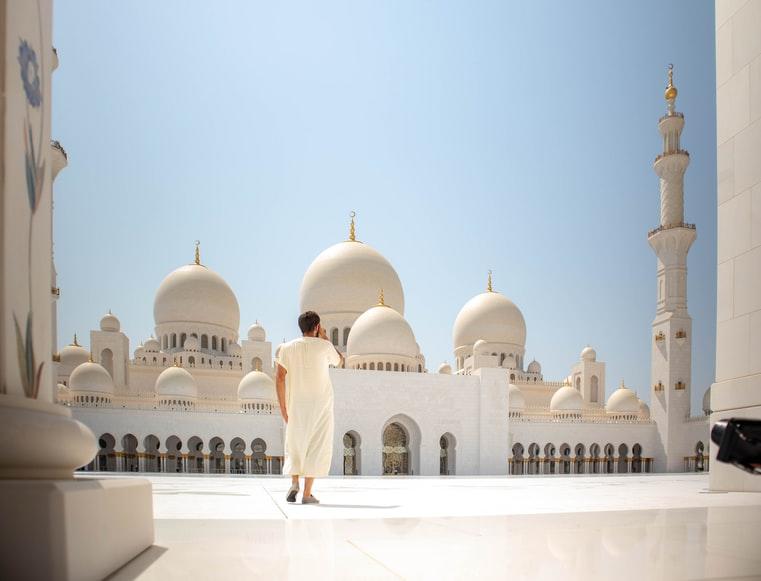 A man in a white thawb standing outside a mosque