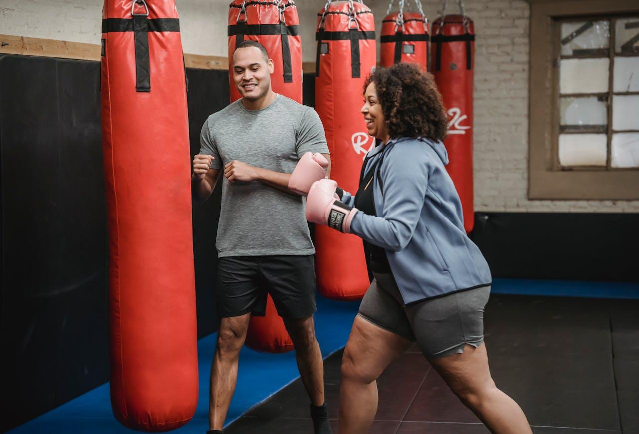 A man helping a woman learn to punch in front of a boxing bag.