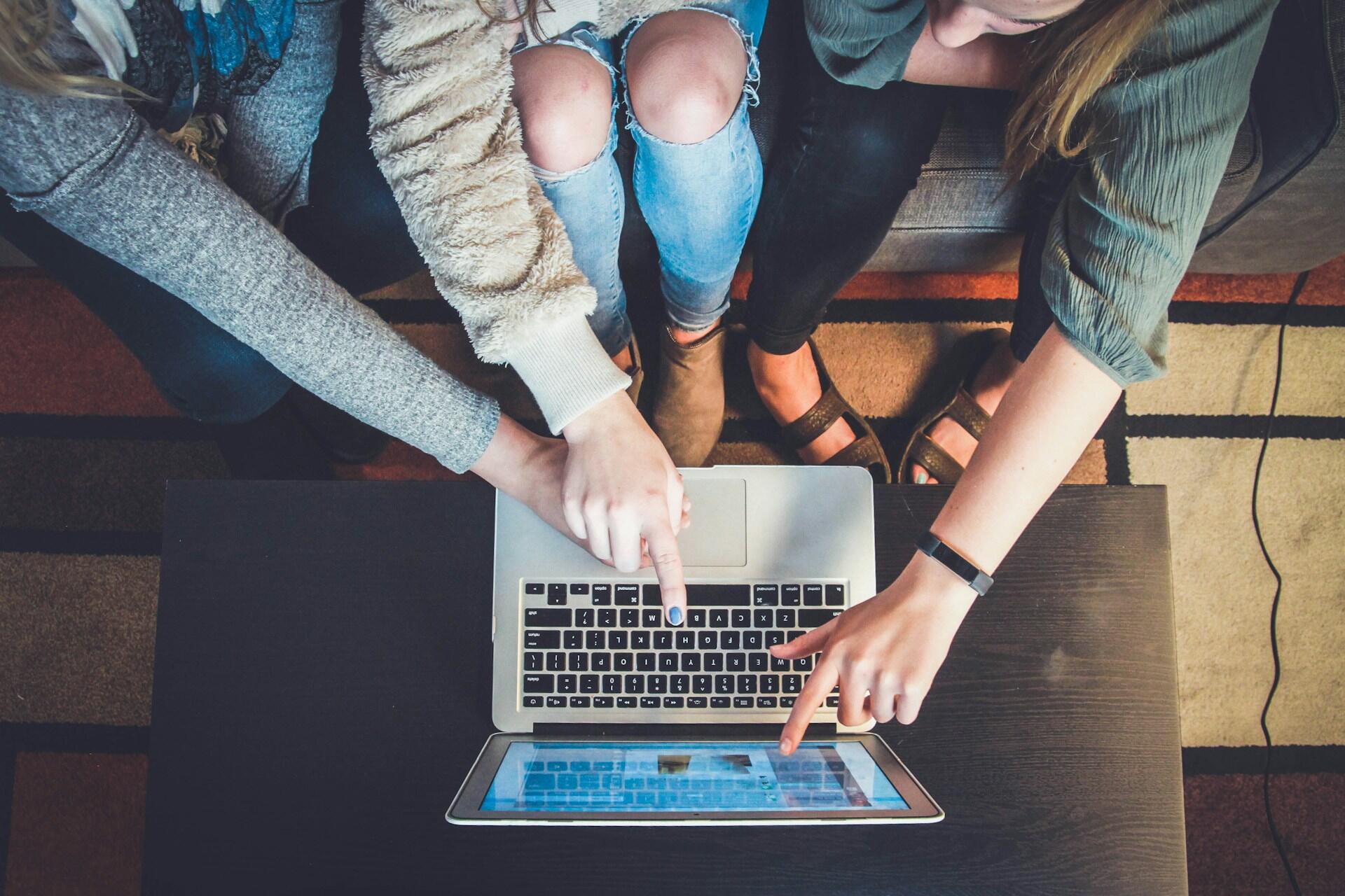 three people sitting around a laptop pointing at the screen
