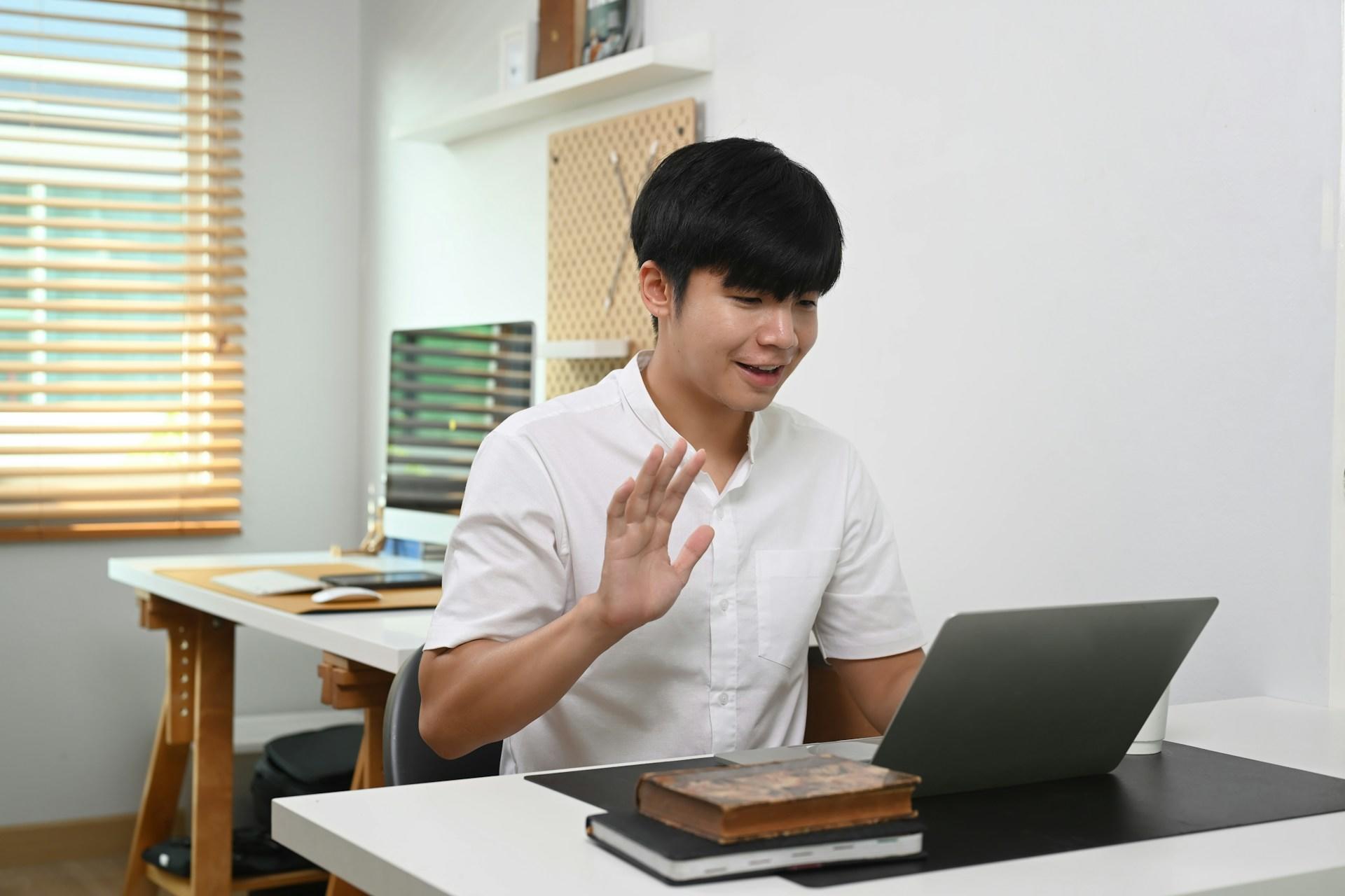 A guy with his hand raised in front of the computer.