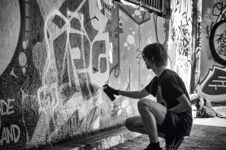 A guy spray painting graffiti on a wall