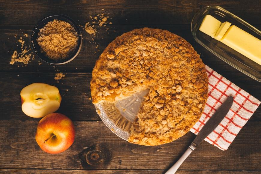 Delicious apple pie placed on the table along with butter and apples