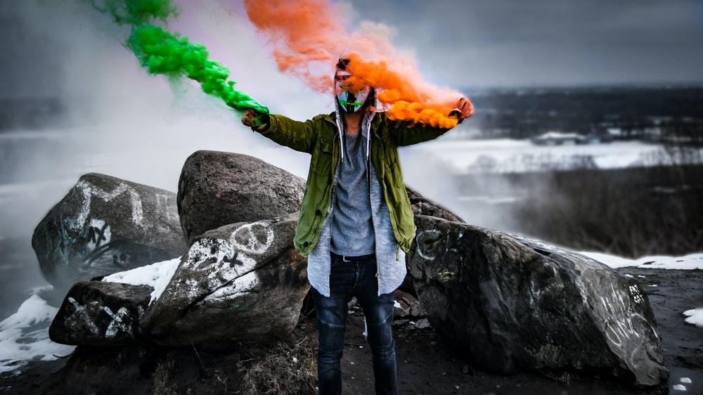 A man holding orange and green smoke flares, representing the Irish flag