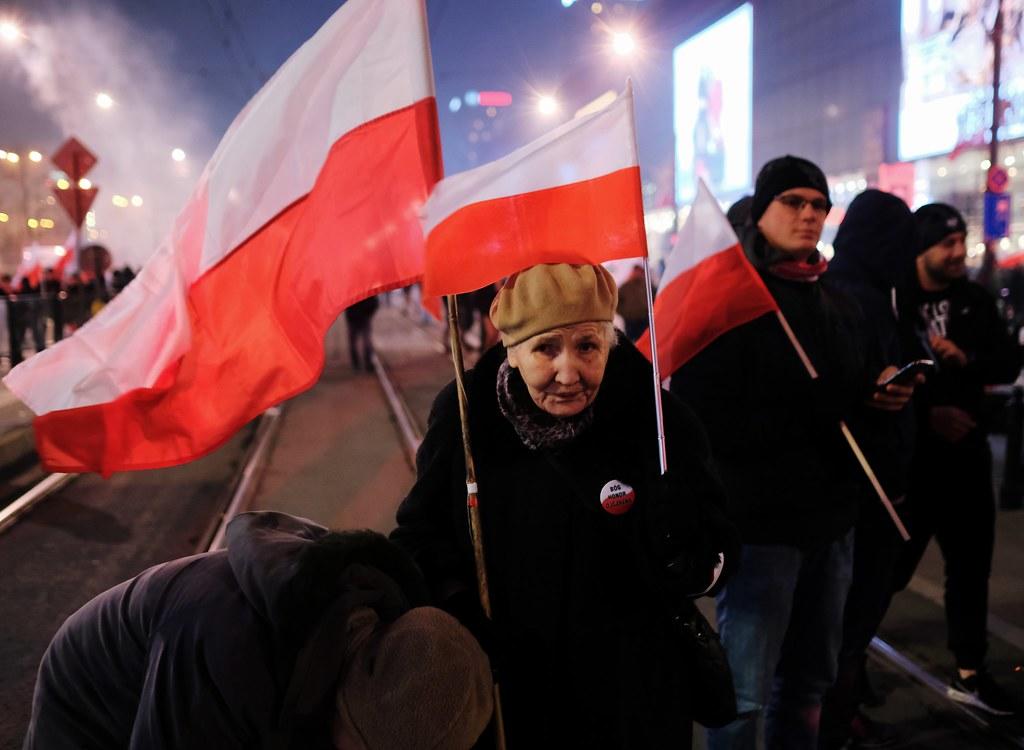 An old lady holding two Polish flags