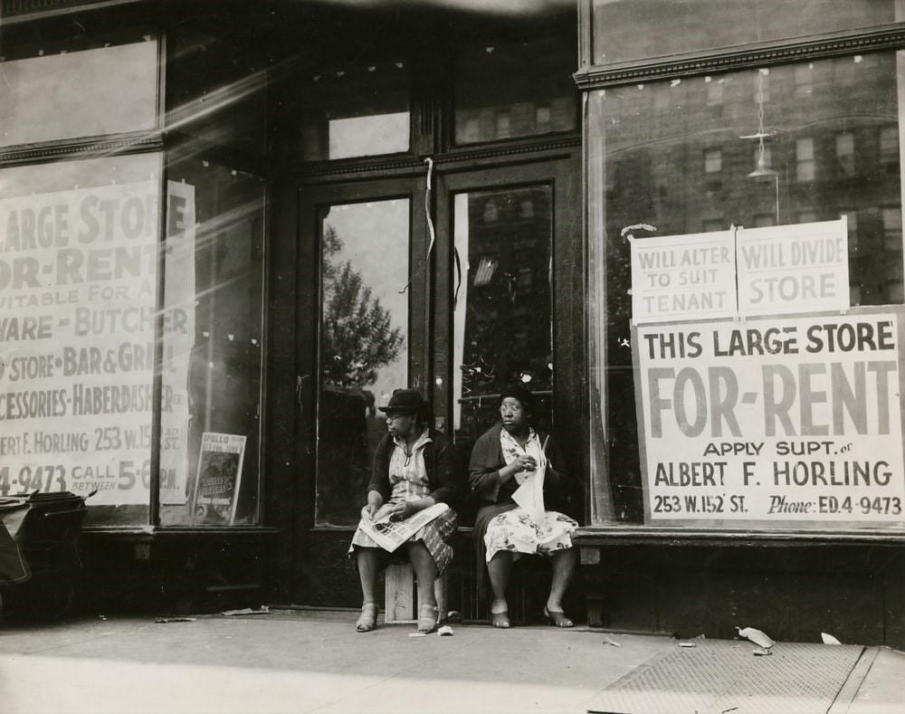 Two black women sitting in front of a store