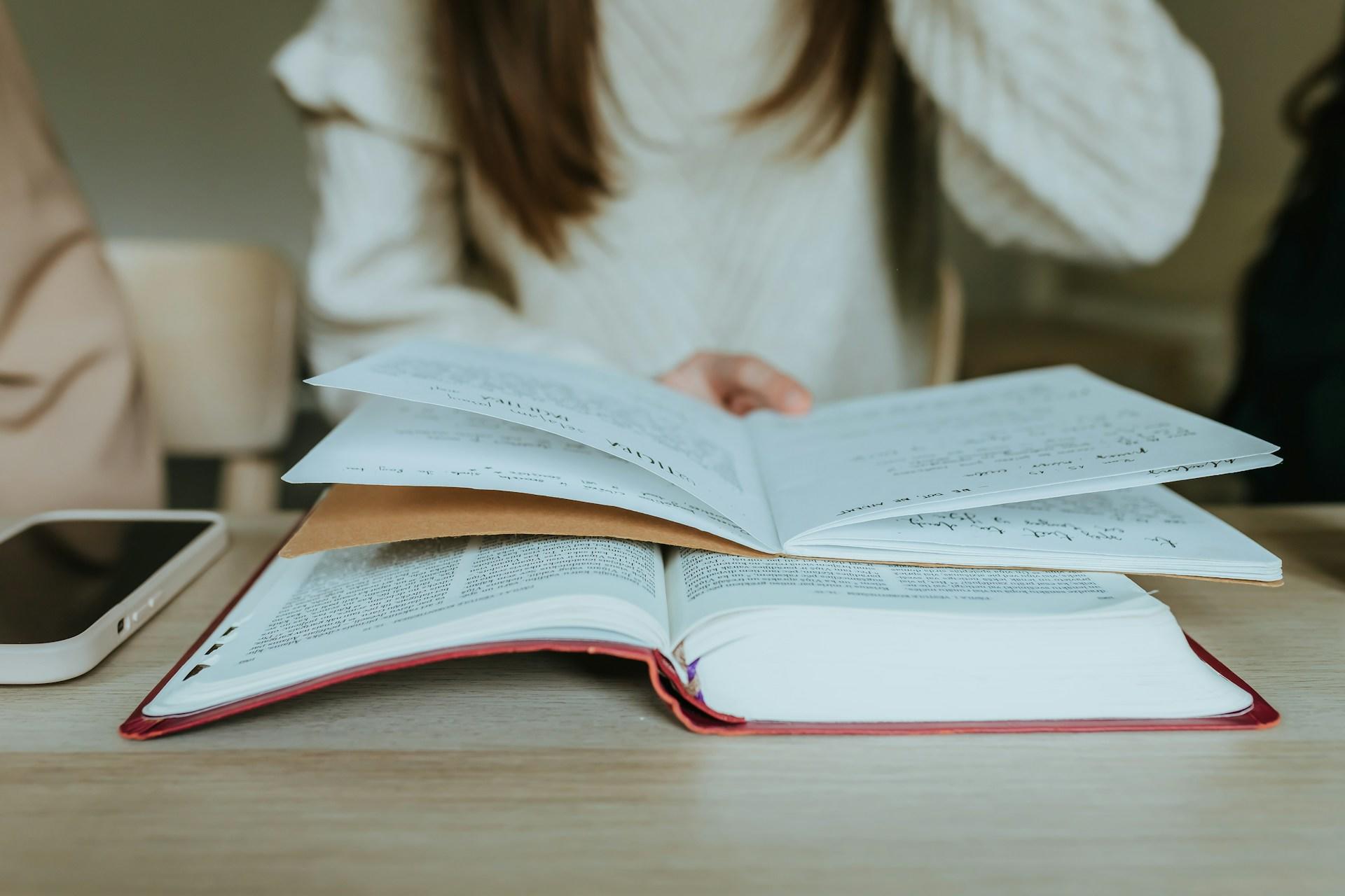 Someone holding a notebook and studying from a book.