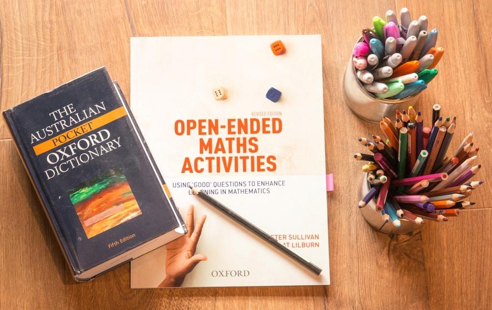 Color pencils, markers, a math activity book, and a pocket dictionary on a table